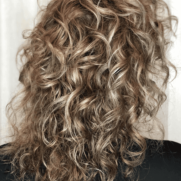 Curly, voluminous hairstyle with soft, defined waves on light brown hair.